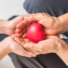 Older adult hands and caregiver hands holding red heart 